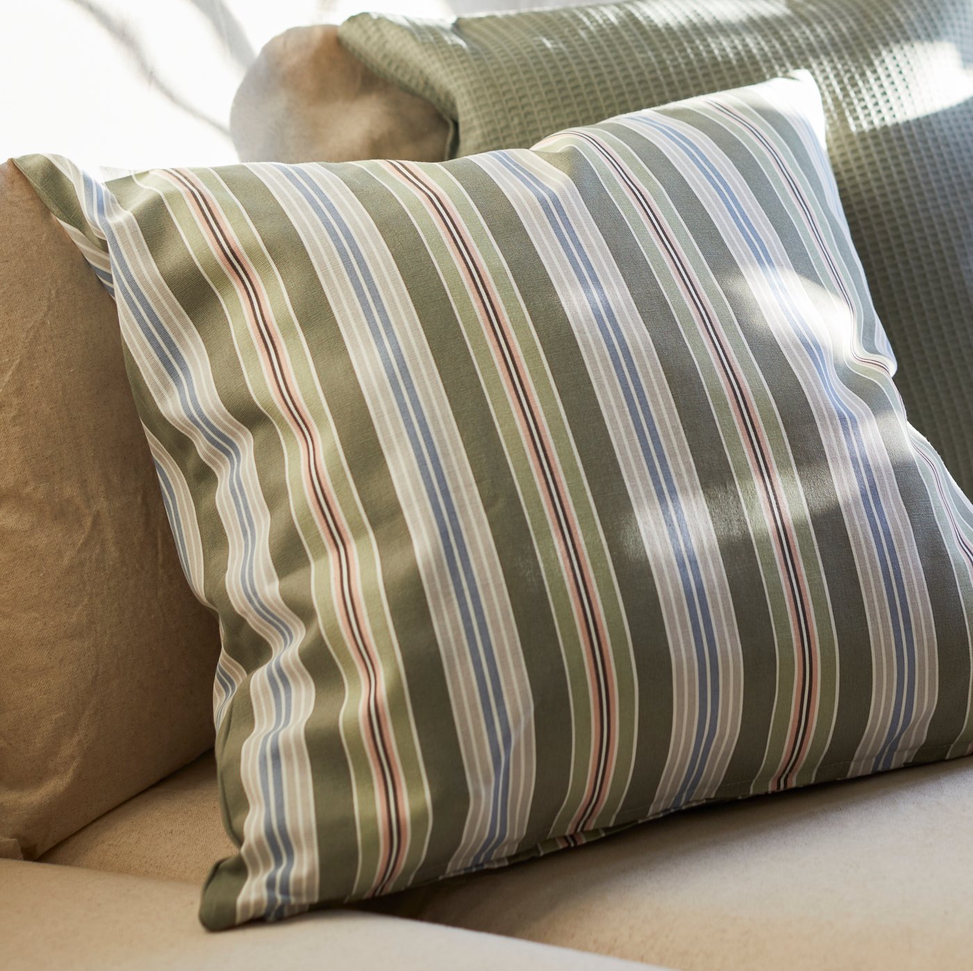 Kusyen di dalam sarung kusyen LINGONOXBÄR berwarna hijau/berjalur-jalur terletak di atas tempat duduk sofa BACKSÄLEN berwarna neutral.