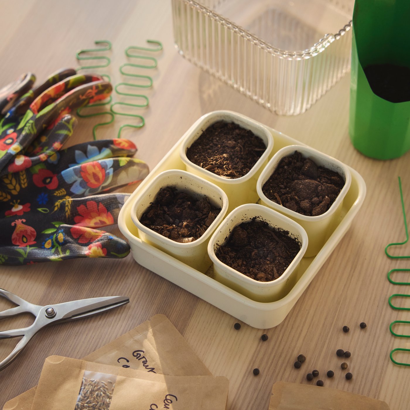Small pots filled with soil on a table surrounded by gardening gloves, scissors, seed packets, and plant supports.