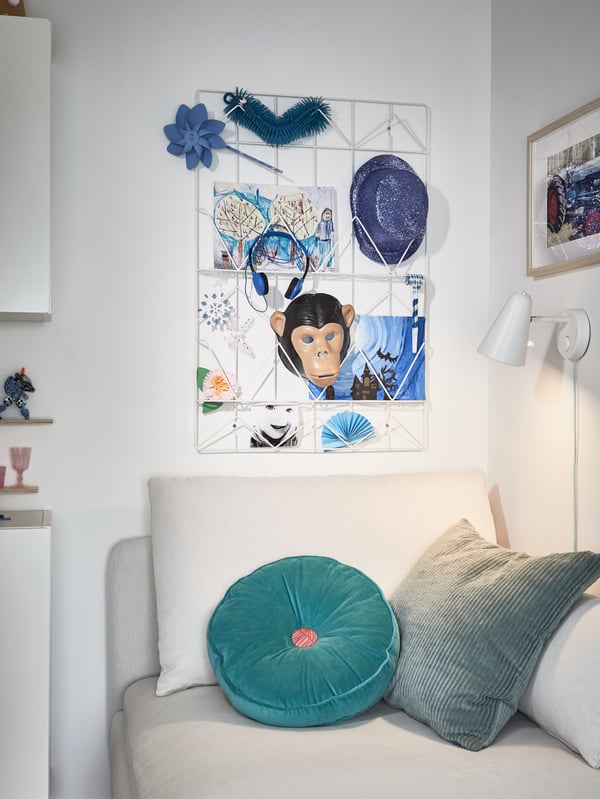 Eine Notiztafel mit blauen Zeichnungen und Utensilien, unter anderem mit einem beigefarbenen Sitzelement, türkisfarbenen Kissen und einer weißen Wandleuchte.