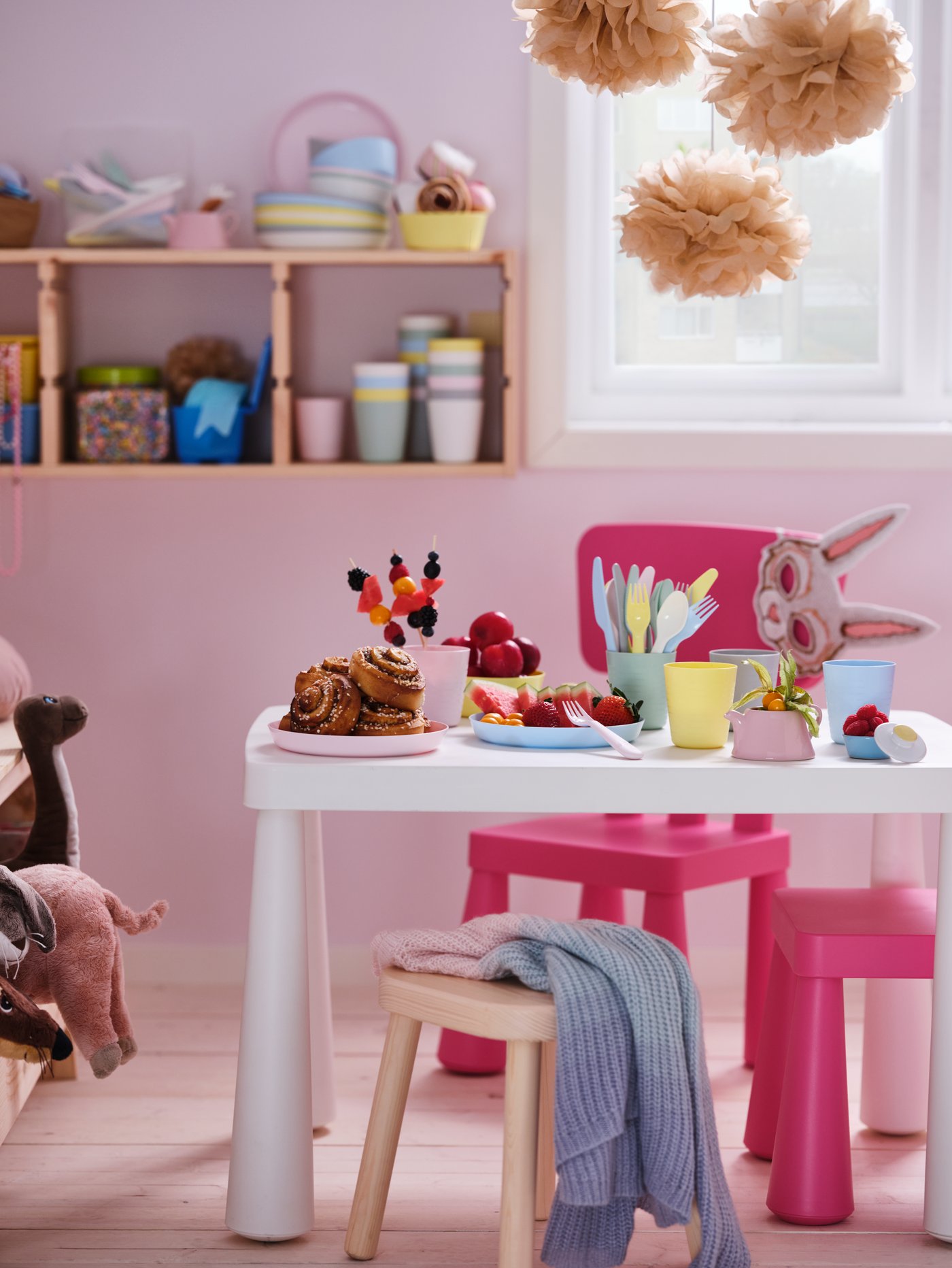 A pastel room with pink MAMMUT children’s chairs around a white MAMMUT children’s table set with colourful snacks.