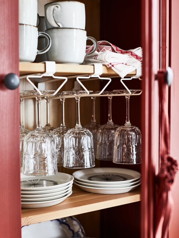 Some PÅLYCKE multi-purpose clip-on racks attached to shelving that holds diverse plates, cups, glasses and tea towels.