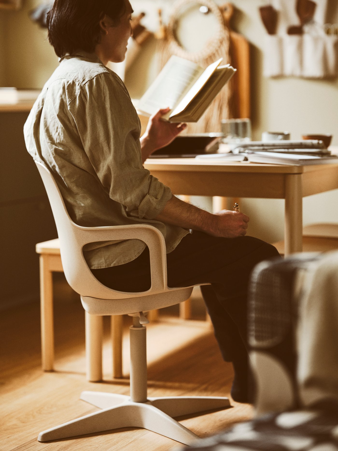 A dining area with a person reading a book while sitting at a RÖNNINGE extendable table in a white-beige ODGER swivel chair.