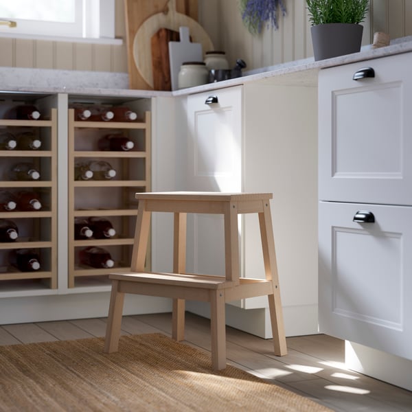 Un tabouret en bois se trouve à côté d’un comptoir avec une armoire de couleur pâle et un range-bouteilles rempli de bouteilles de vin.