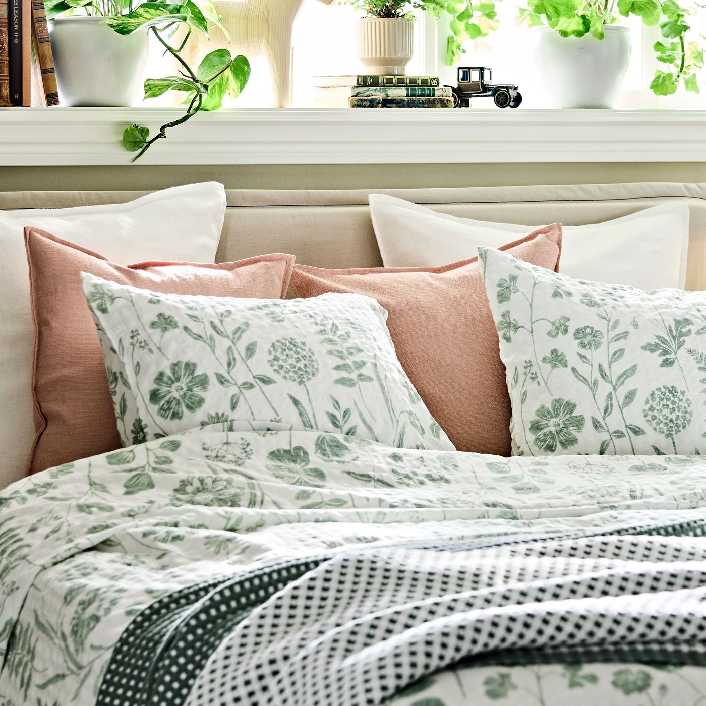 A bed, neatly made with NÅLBJÖRNBÄR duvet cover and pillow cases and decorative pillows in white.