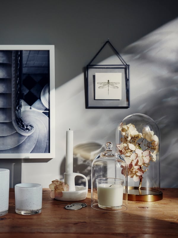 A large clear glass vase sits on a stock of books. Next to this a carafe with glasses  in a traditional style. 