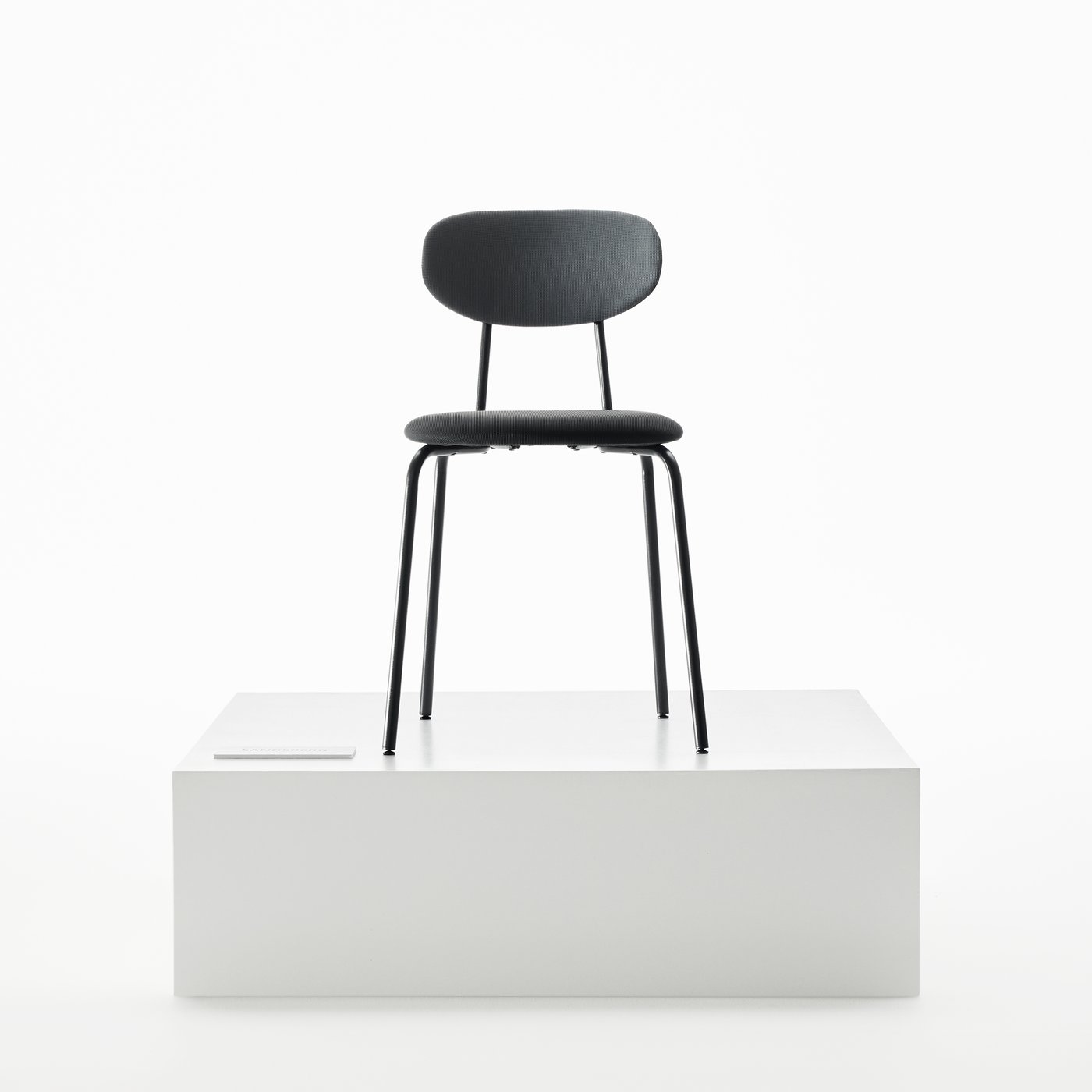 Chaise SANDSBERG en anthracite/Remmarn anthracite posée sur un socle blanc d’une façon qui met en valeur son design minimaliste.