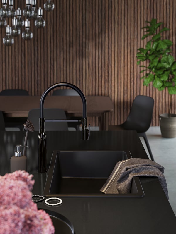 A black inset sink and tap on a black worktop on the kitchen island, a grey tea towel, black and white bracelets.