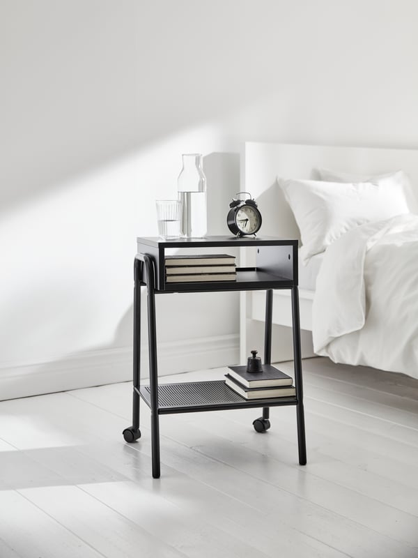 An IDANÄS upholstered bed covered in ÄNGSKLOCKA bed linen, with a bedside table, in front of a white DYTÅG curtain.