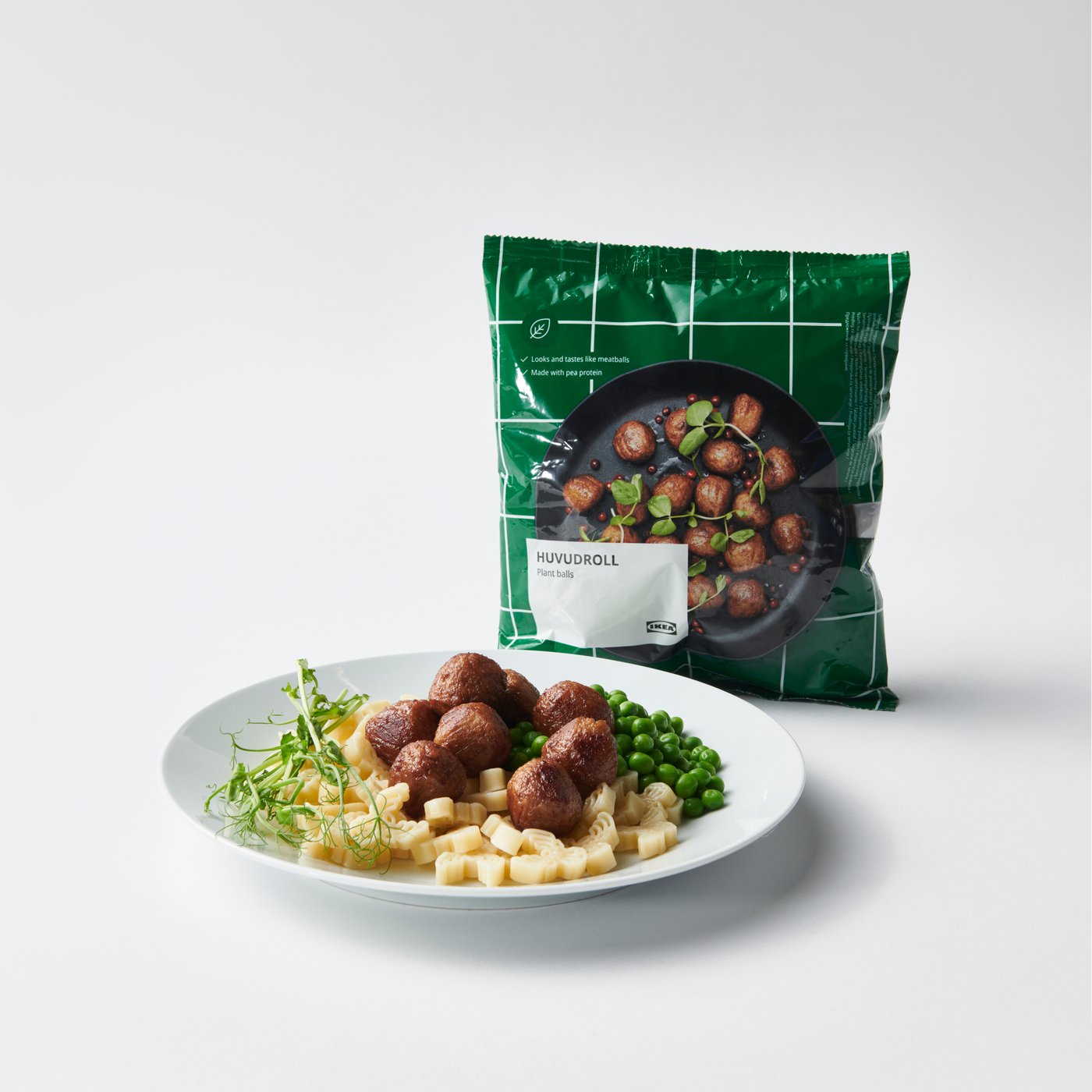 Närbild av en vit tallrik med HUVUDROLL växtbaserade bullar serverade med pasta och ärtor. HUVUDROLL-förpackningen i bakgrunden.