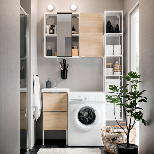 Imagen frontal de un espacio de baño con una lavadora frente al muro del fondo y un mueble ENHET con cajas organizadoras junto a una ventana, al lado derecho.