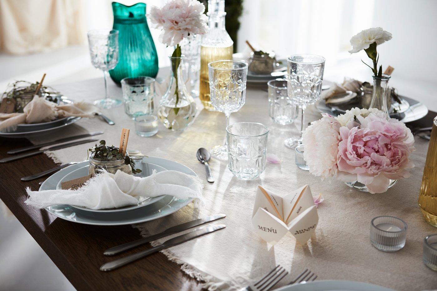 Et festligt bord dækket til en formel lejlighed med en let dug, fine glas, tallerkener, bestik og blomsterdekorationer.