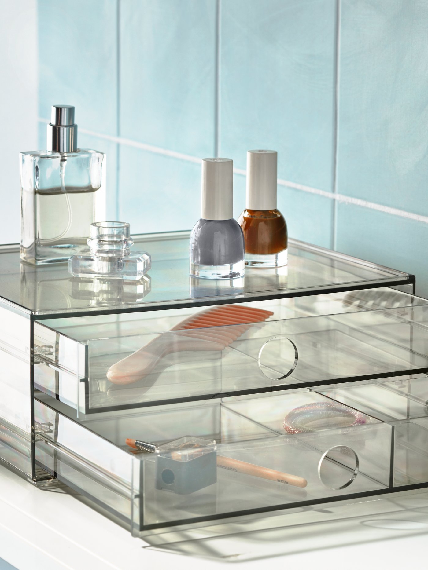 Contenedores transparentes con esmaltes de uñas y un perfume encima de ellos.