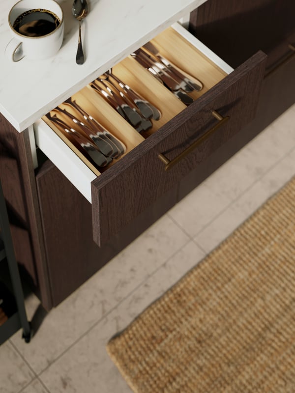 A kitchen with SINARP drawers and doors and a black pendant lamp. Next to a window is a rolling table with bowls.