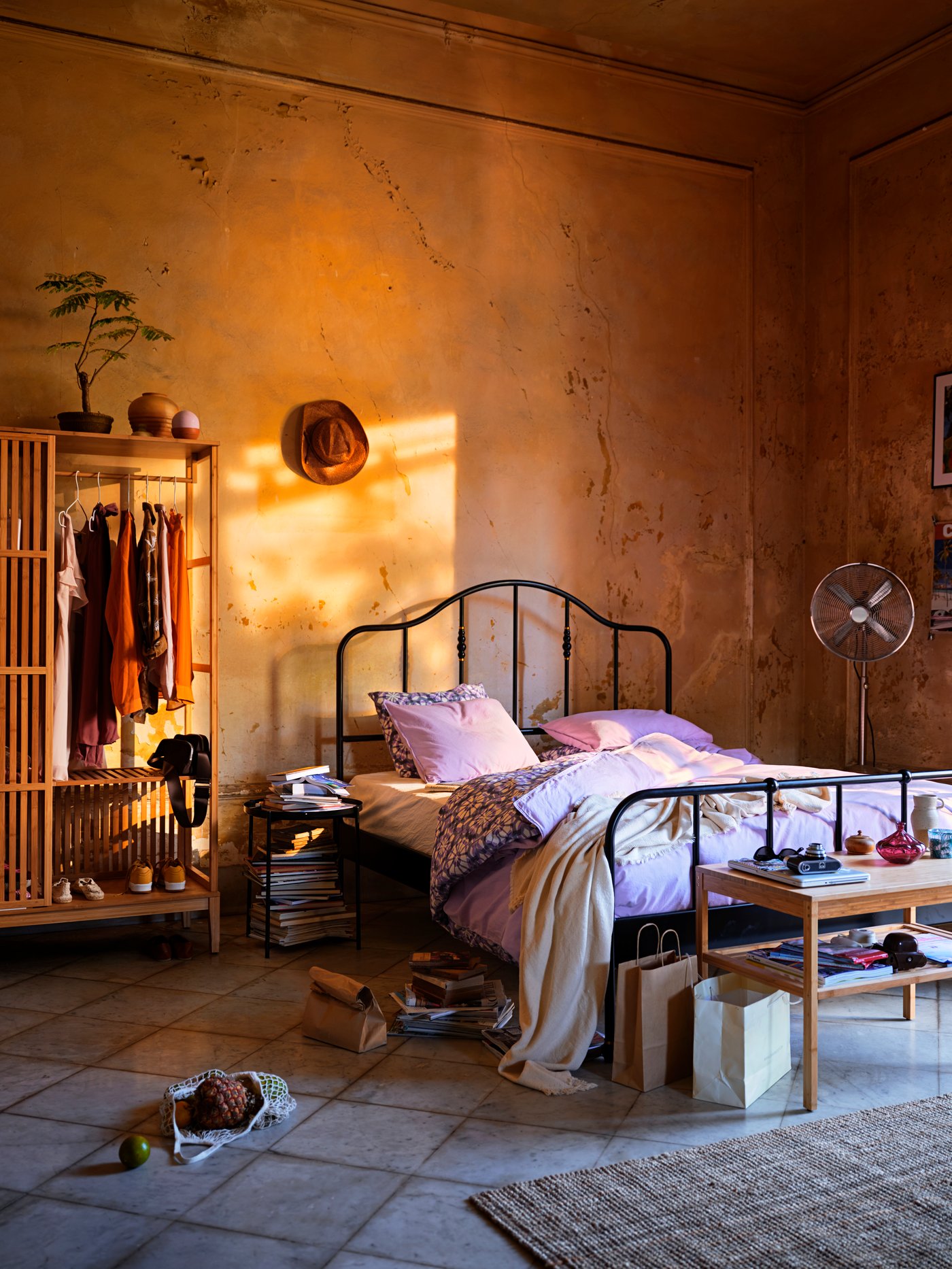 Schlafzimmer mit einem schwarzen Metallbett. Am Bettende steht eine schlichte Bettbank aus Holz. Neben dem Bett ist ein halb offener Kleiderschrank.