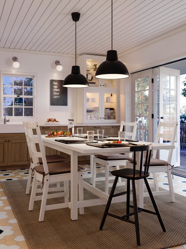 A white NORDVIKEN table with five chairs laid for a meal in the middle of a kitchen. Two SKURUP pendants hang overhead.