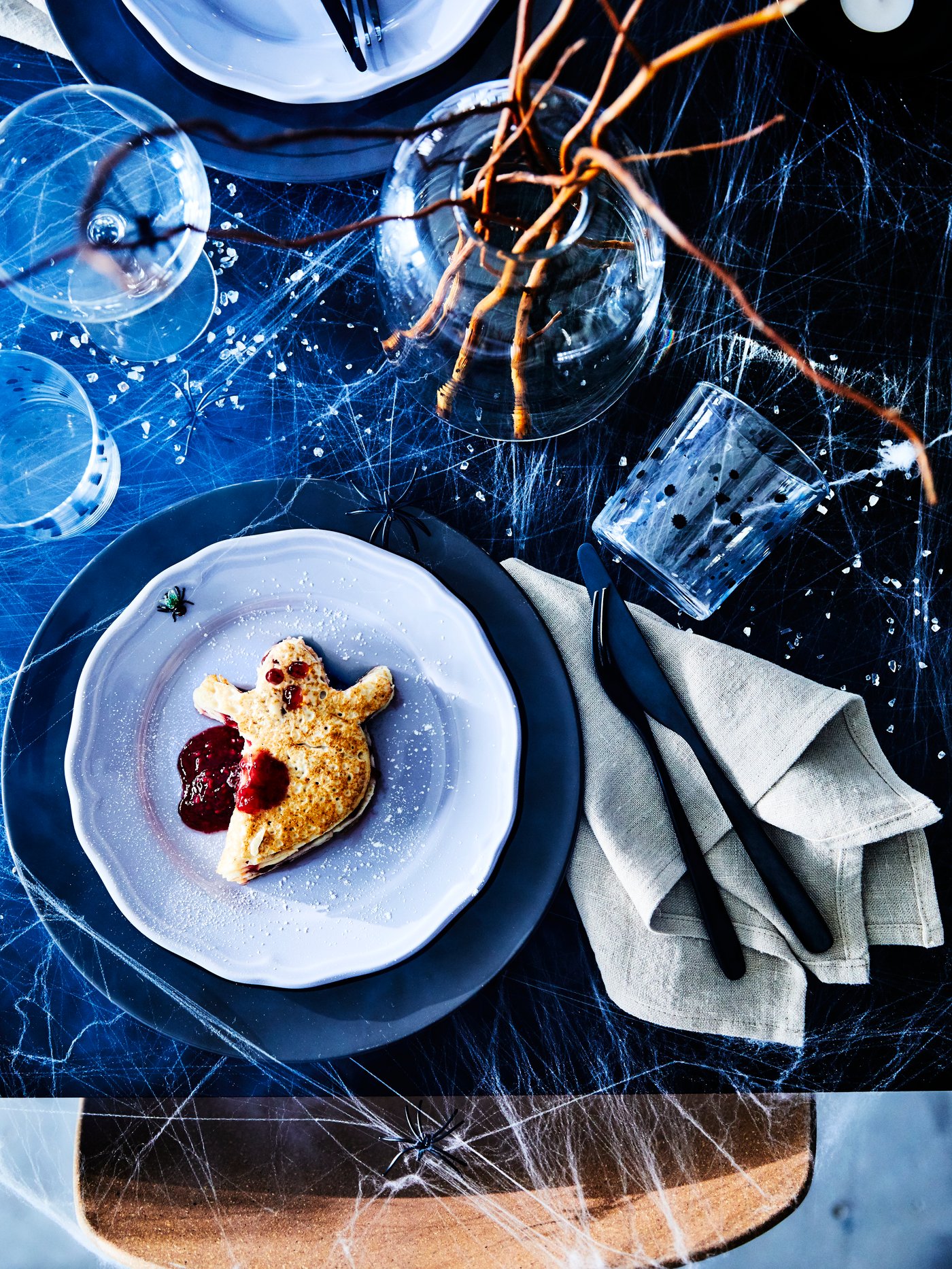 Elegant dukning med blå tallrikar, dessert, bestick, servett och dekorativa spindelnät.