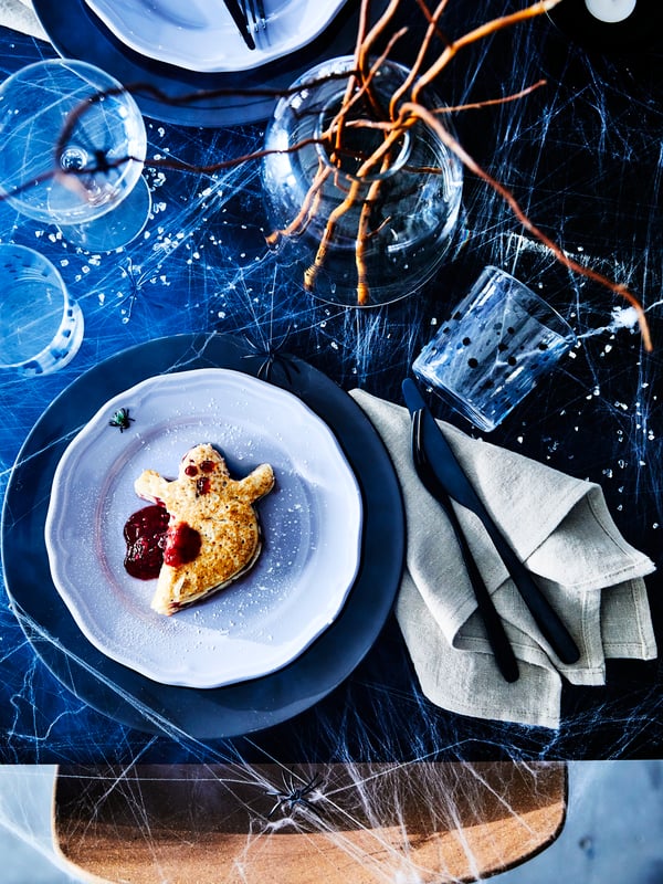 En pannkaka i form av ett spöke ligger på en UPPLAGA assiett på ett dukat bord.
