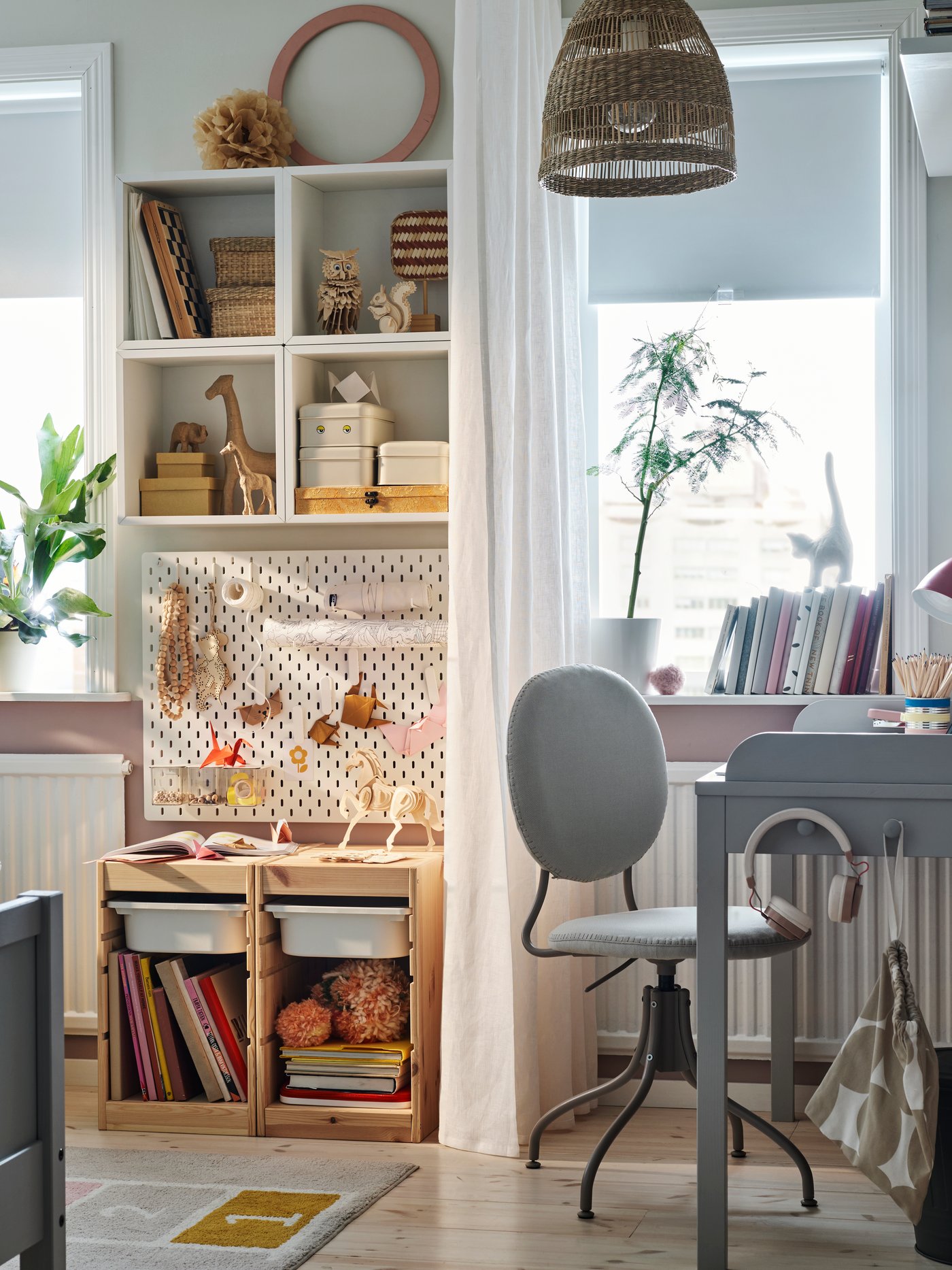 A cosy children’s bedroom with a grey SMYGA desk beside a window with a white curtain and a SKÅDIS pegboard behind it.