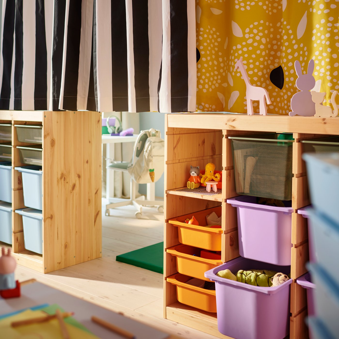 Deux étagères TROFAST au milieu d’une chambre d’enfant partagée avec un rideau différent en haut de chaque.