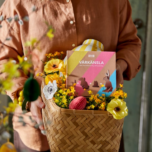 EN eprson holder en kurv fyldt med kunstige blomster og en chokolade påskekanin