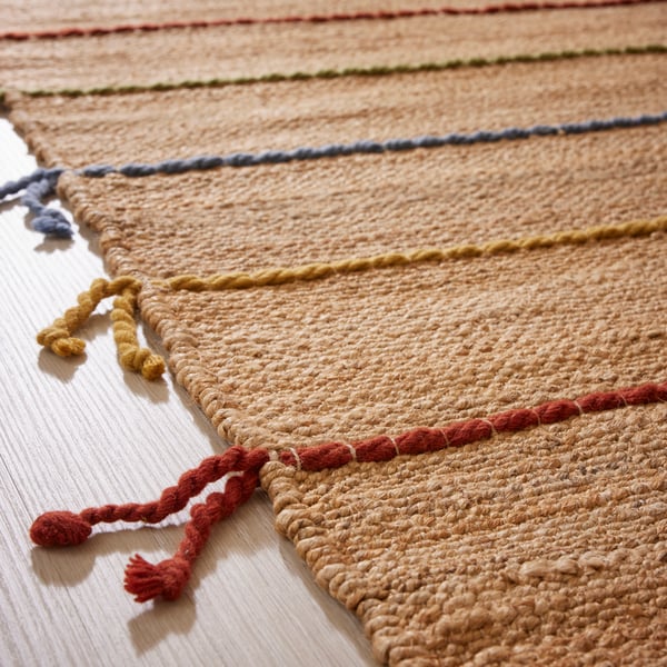A RAKLEV flatwoven rug, made of jute with woollen stripes and tassels of different colours, lies on a floor.