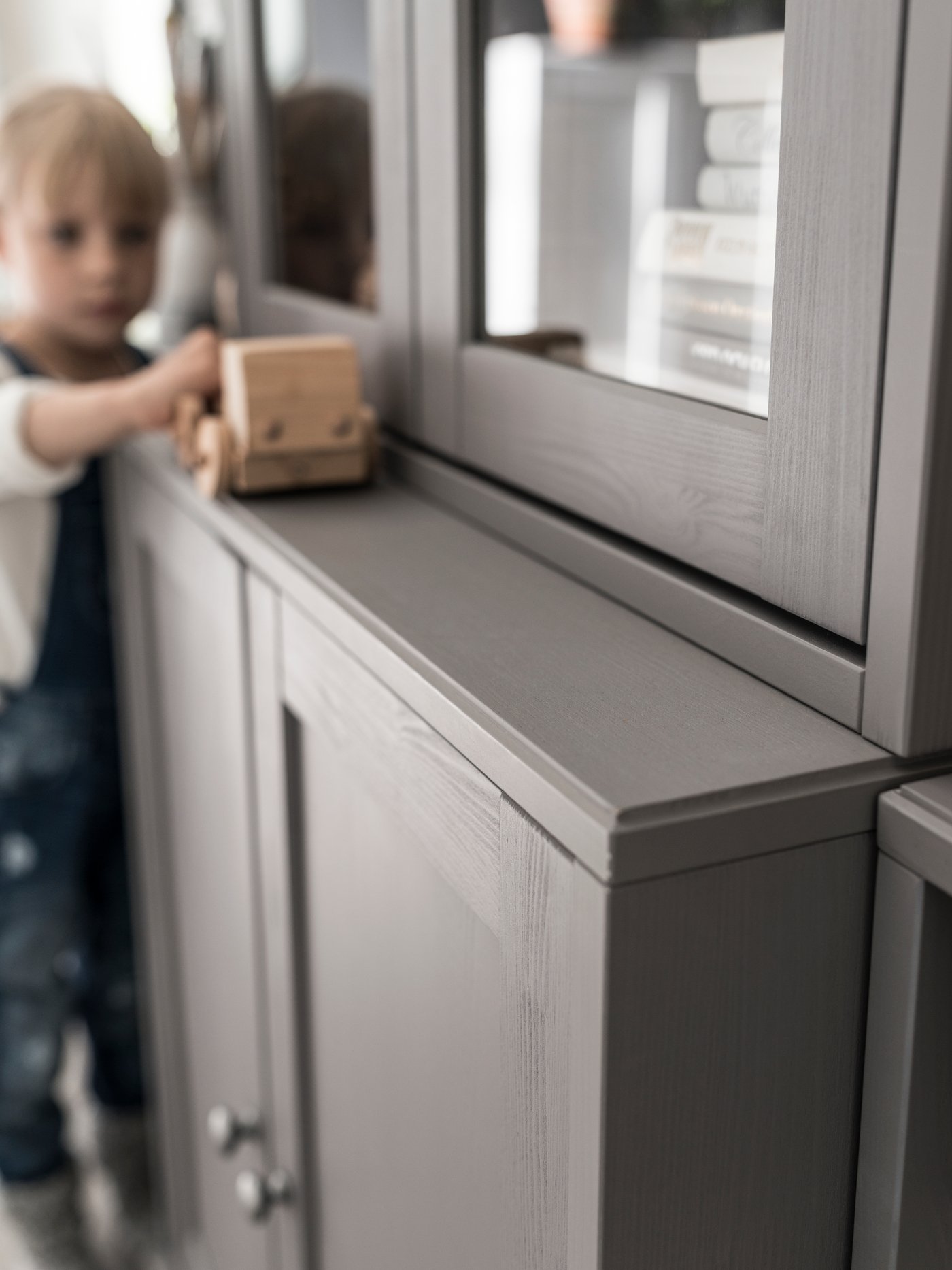 Un enfant joue avec un camion en bois sur le rebord d’un rangement avec portes vitrées HAVSTA.