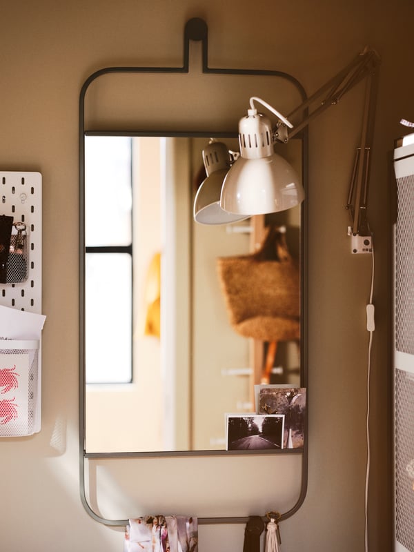 A wall-hanging GRANVÅG mirror reflecting part of a room with a TERTIAL work lamp mounted to the side.