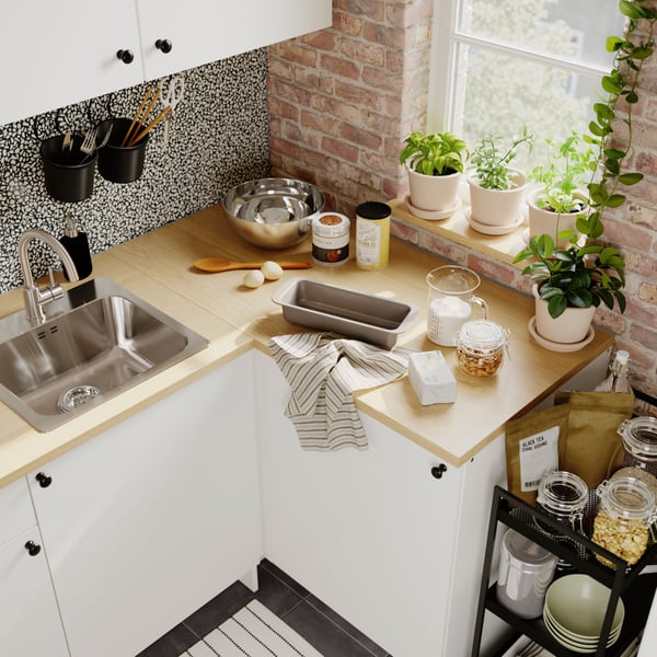 A bright kitchen scene featuring a white KNOXHULT corner base cabinet, plants, and cooking utensils near a sunny window.