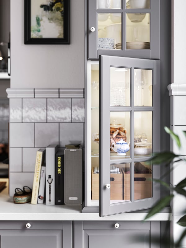 Base cabinets with gray BODBYN fronts, wall cabinets with glass doors and integrated lighting, plus cookbooks on a worktop.