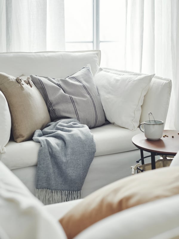 Une pièce lumineuse et aérée avec un fauteuil BACKSÄLEN blanc couvert de textiles, près d’une table de rangement ÄNGESBYN sur laquelle est posée une tasse.