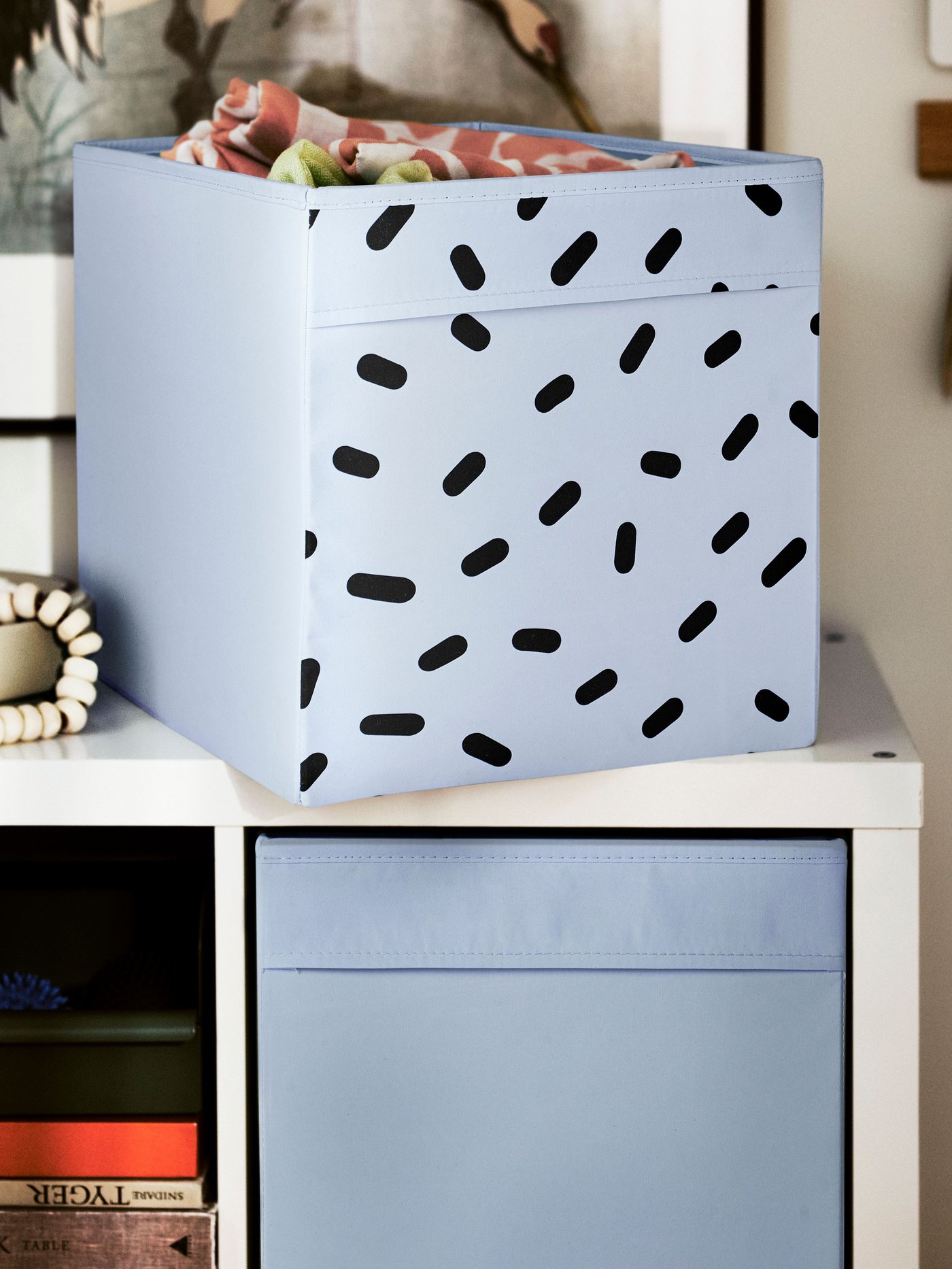 DRÖNA box in blue with black speckled patterns on top of a white KALLAX storage unit. 