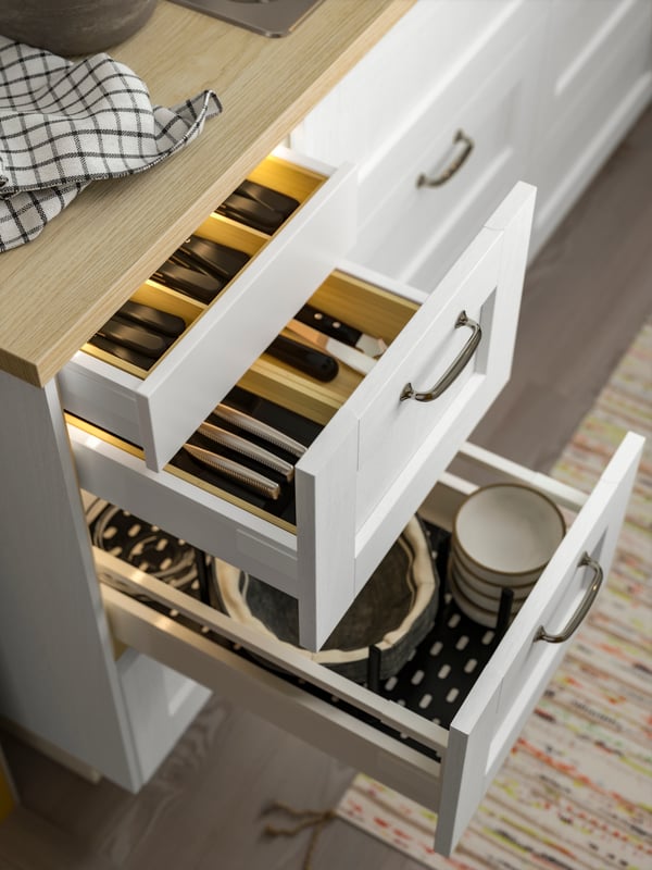 Two drawers with white ENKÖPING fronts are pulled out, one of them has a drawer in a drawer, with kitchen items inside.