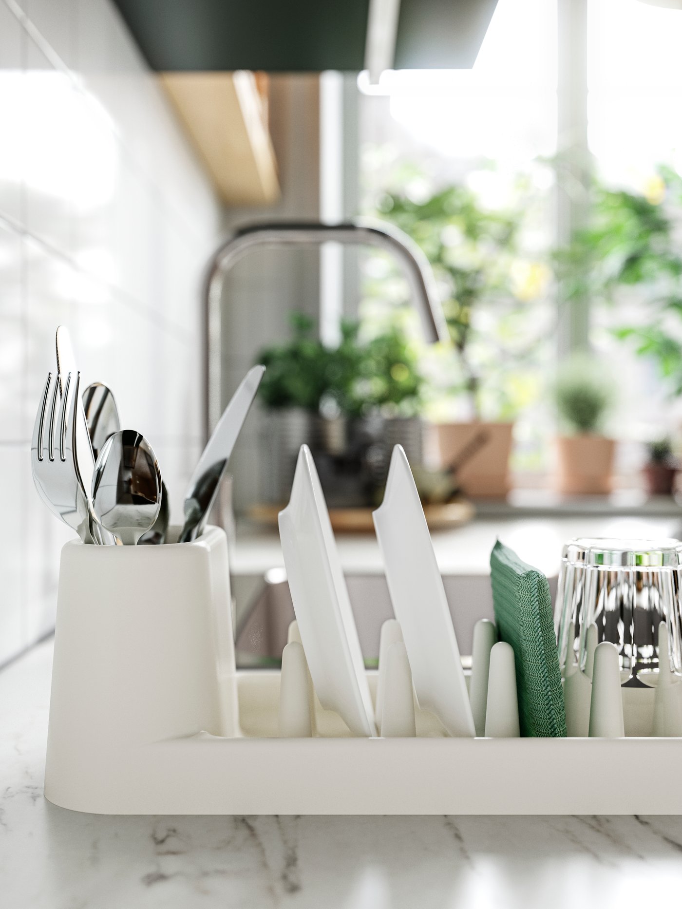 An off-white STÄMLING dish drainer holding a glass, two white plates and cutlery, on a white marble effect/laminate worktop.
