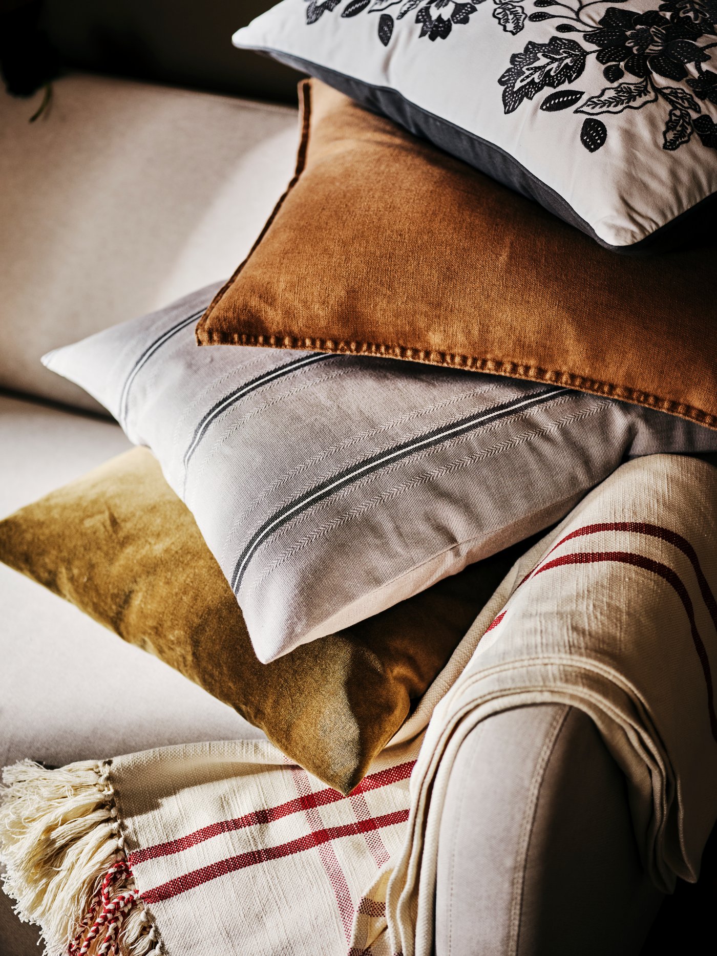 Four cushions, including one in a grey/white STORTIMJAN cushion cover, are piled on a LINANÄS sofa near a throw.