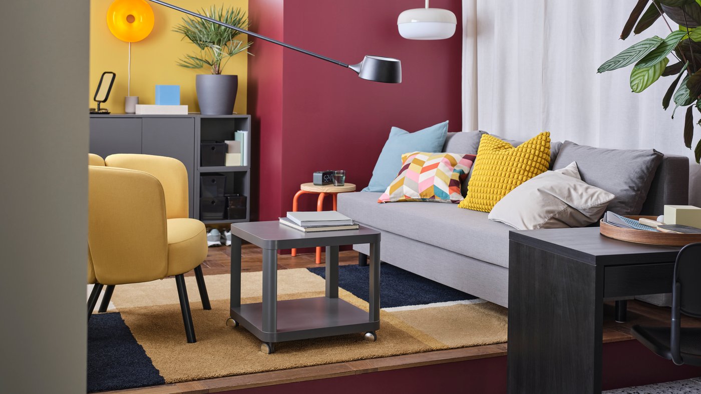 A retro inspired living room with a large grey ÄLVDALEN sofa-bed, yellow armchair, grey coffee table and bold painted walls.