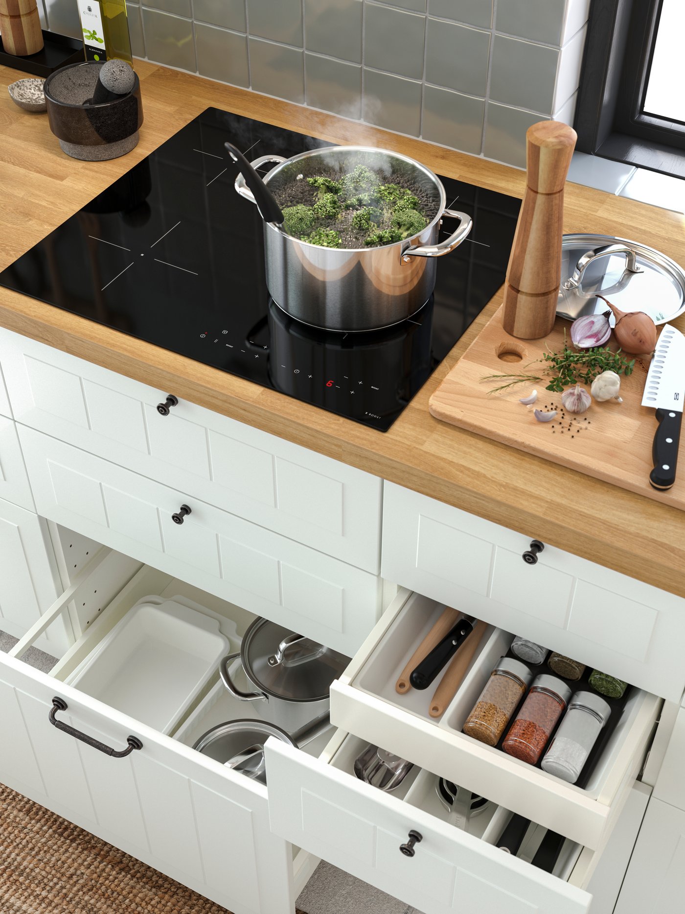 An IKEA 365+ pot with lid on a black induction hob, with open kitchen drawers below with pots, oven dishes and spices inside.
