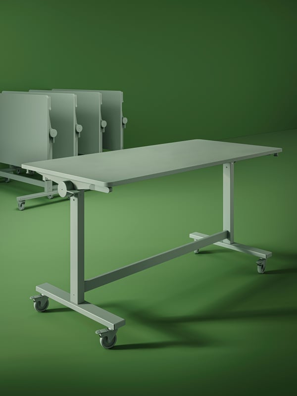 Five green MITTZON foldable tables with castors in a space with green walls and floors. Four of them are folded.