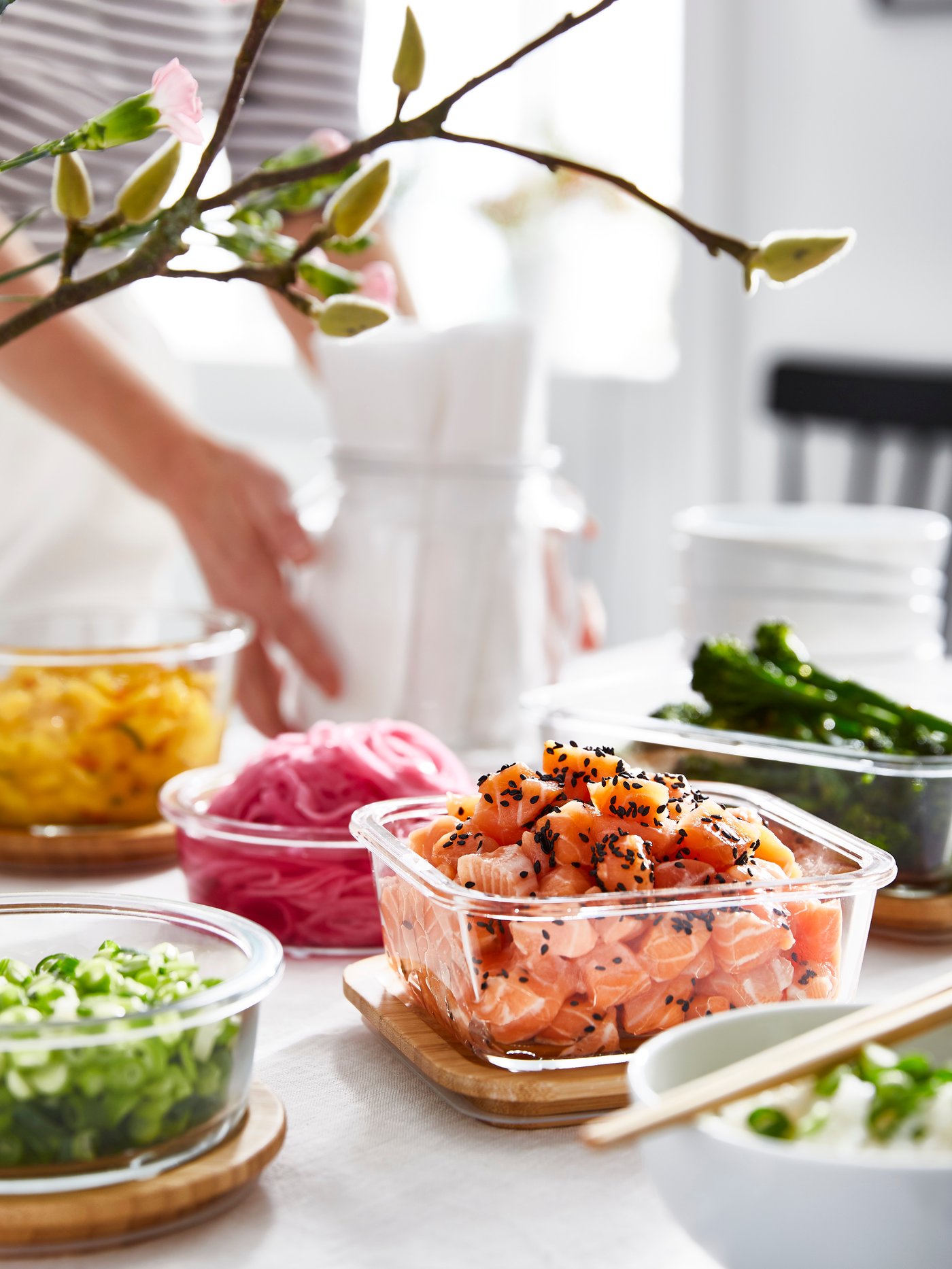 Plusieurs contenants en verre IKEA 365+, remplis de saumon, de différents légumes et de fruits, sont posés sur leurs couvercles en bambou.