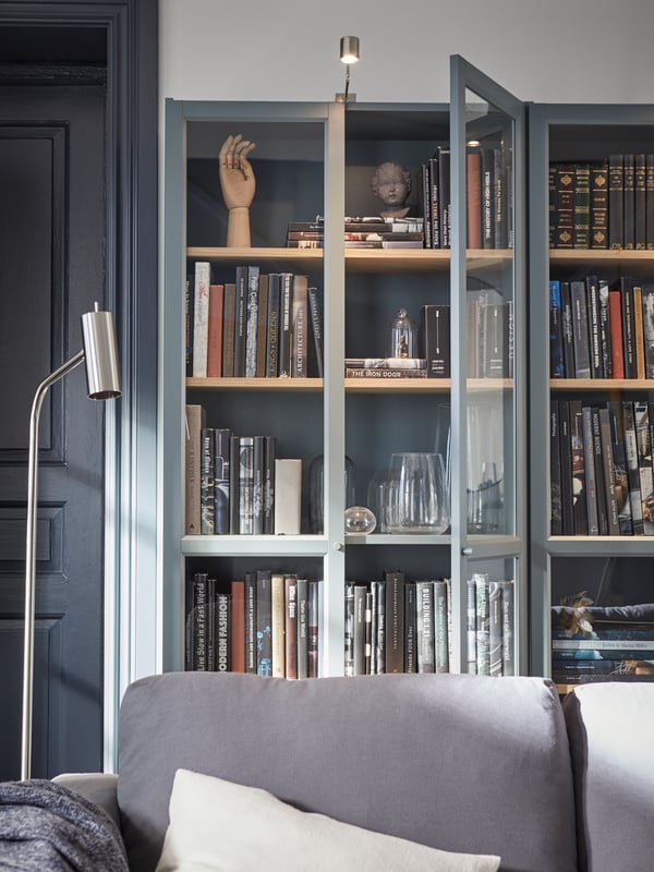 Behind the sofa are gray-turquoise bookcases with glass doors, with books, vases and decorative items in them.