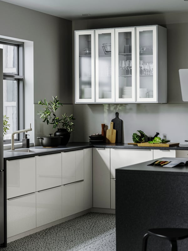Vista frontal de un mueble de cocinas  con puertas HEJSTA de color blanco con vidrios.  En el interior se puede ver una despensa con vajillas.