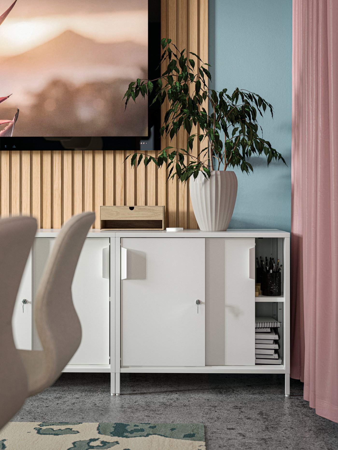 Two white TROTTEN cabinets with sliding doors are on a wall under a big TV screen. An open door shows office supplies inside.