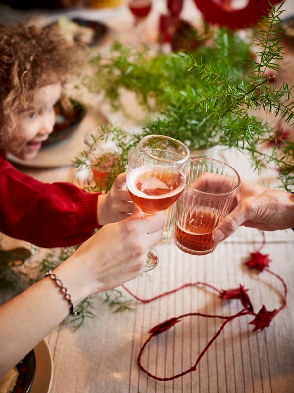 Family raising a toast at Christmas time with ÄNKEBLOMSTER glassware and striped VIPPSTARR tablecloth.