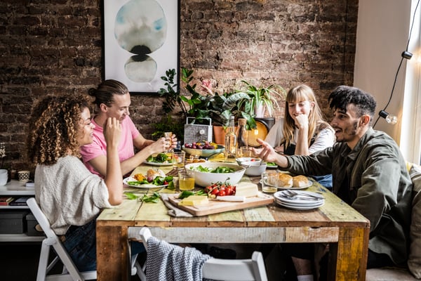 Plusieurs personnes partagent un repas autour d’une table en bois et discutent.