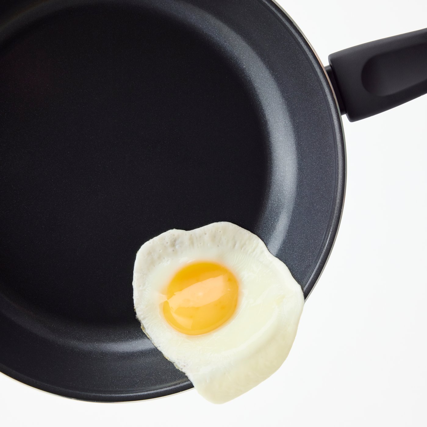 A fried egg is sliding out of a TAGGHAJ non-stick frying pan.