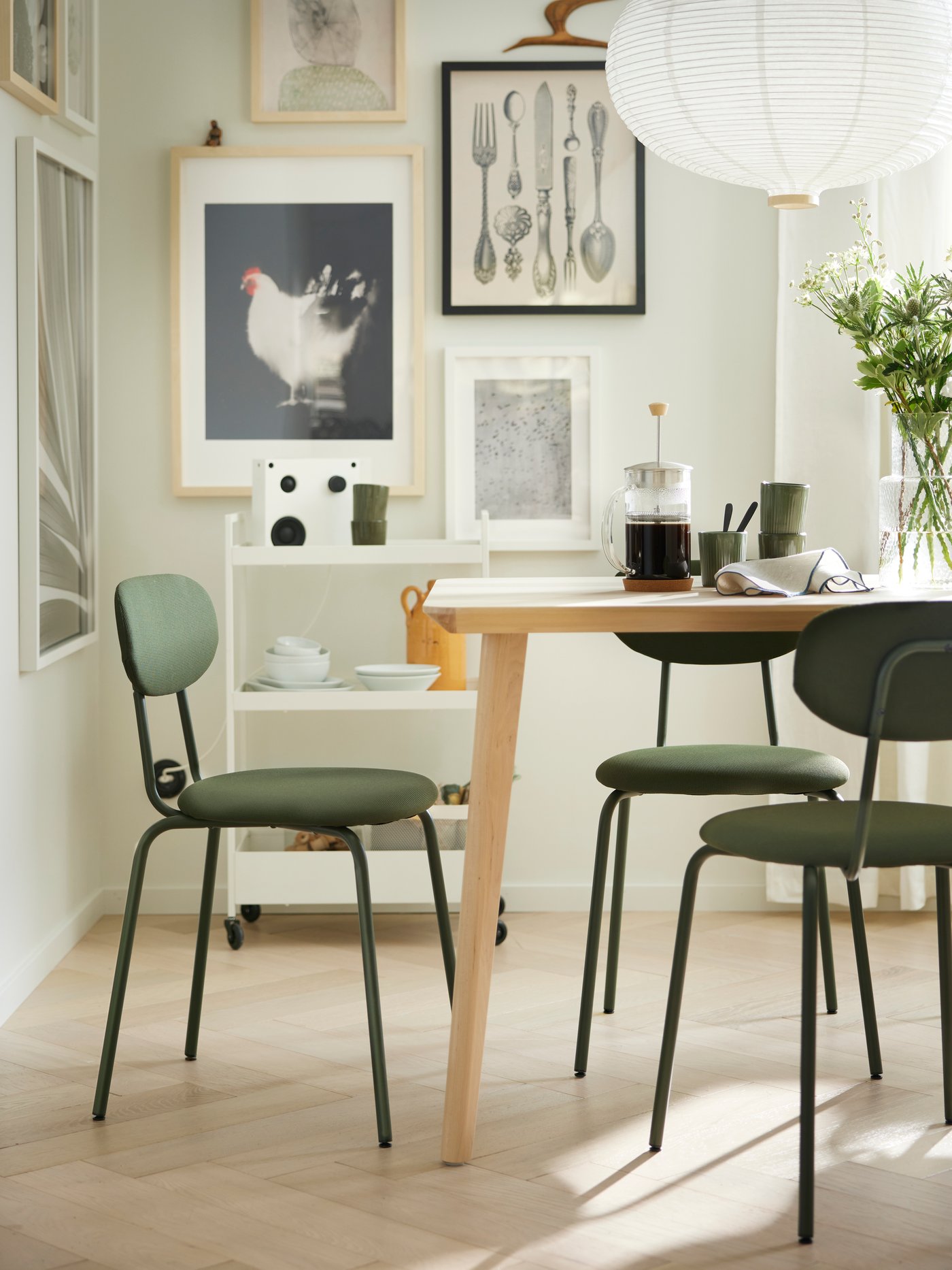 Una mesa de comedor con una cafetera y otros artículos para desayunar. La mesa tiene 3 sillas de comedor ÖSTANÖ verdes.