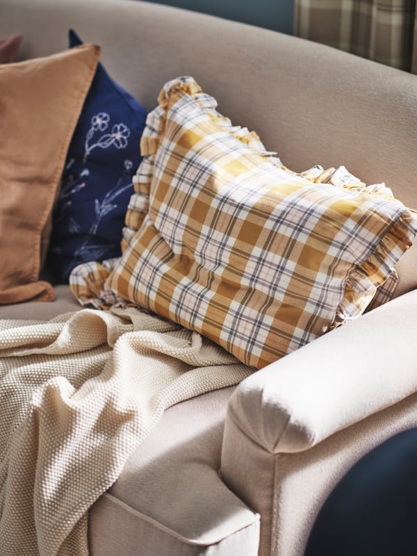A pillow in a PARKOLVON multicolour/check pillowcase lies on an ESSEBODA sofa with a HUMLEMOTT throw and two cushions.