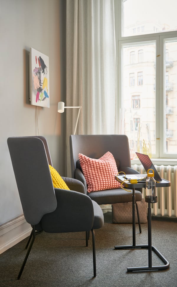 Mysig sittgrupp vid fönster med två grå BINGSTA fåtöljer, med en rosa och en gul kudde, framför ett GJÖRKÅSEN laptopbord.  dekorativa kuddar i ett modernt vardagsrum.