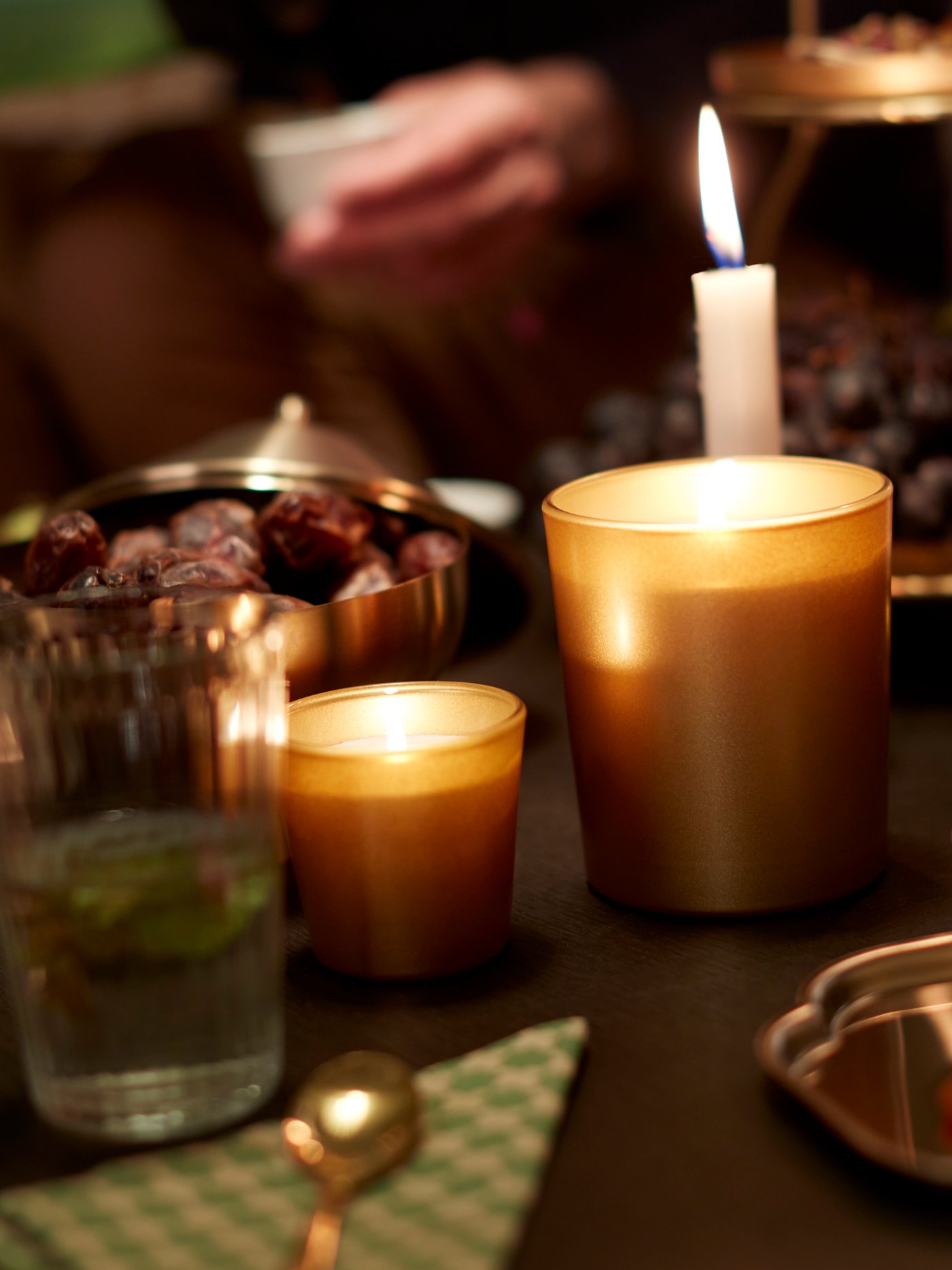 A glowing GOKVÄLLÅ scented candle in glass, sandalwood patchouli scent, in a cosy living room setting.