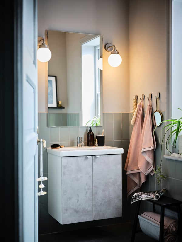 A bathroom with an ENHET bathroom cabinet, a VILTO storage stool, VIKFJÄRD towels hanging and FRIHULT lamps on the wall.