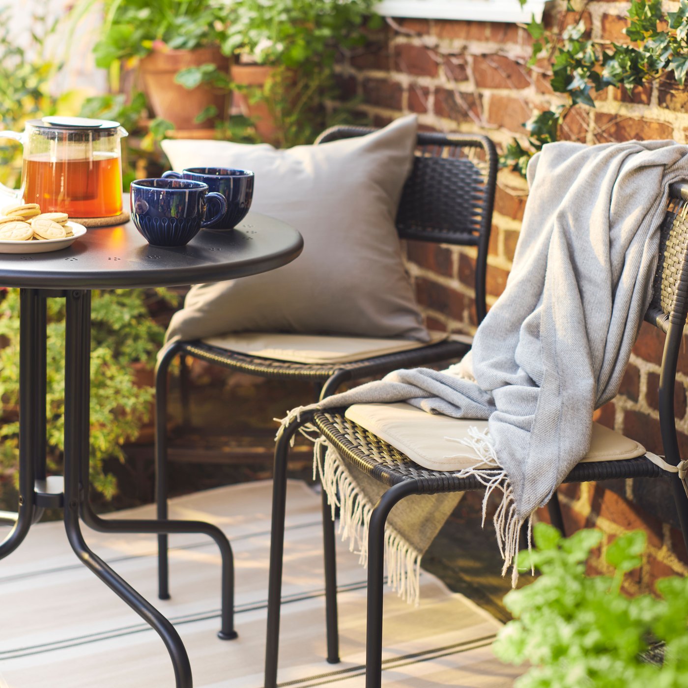 VIRKLUND outdoor rug in a small balcony area with a LACKO dining table set with two outdoor chairs, some cushions and throws.